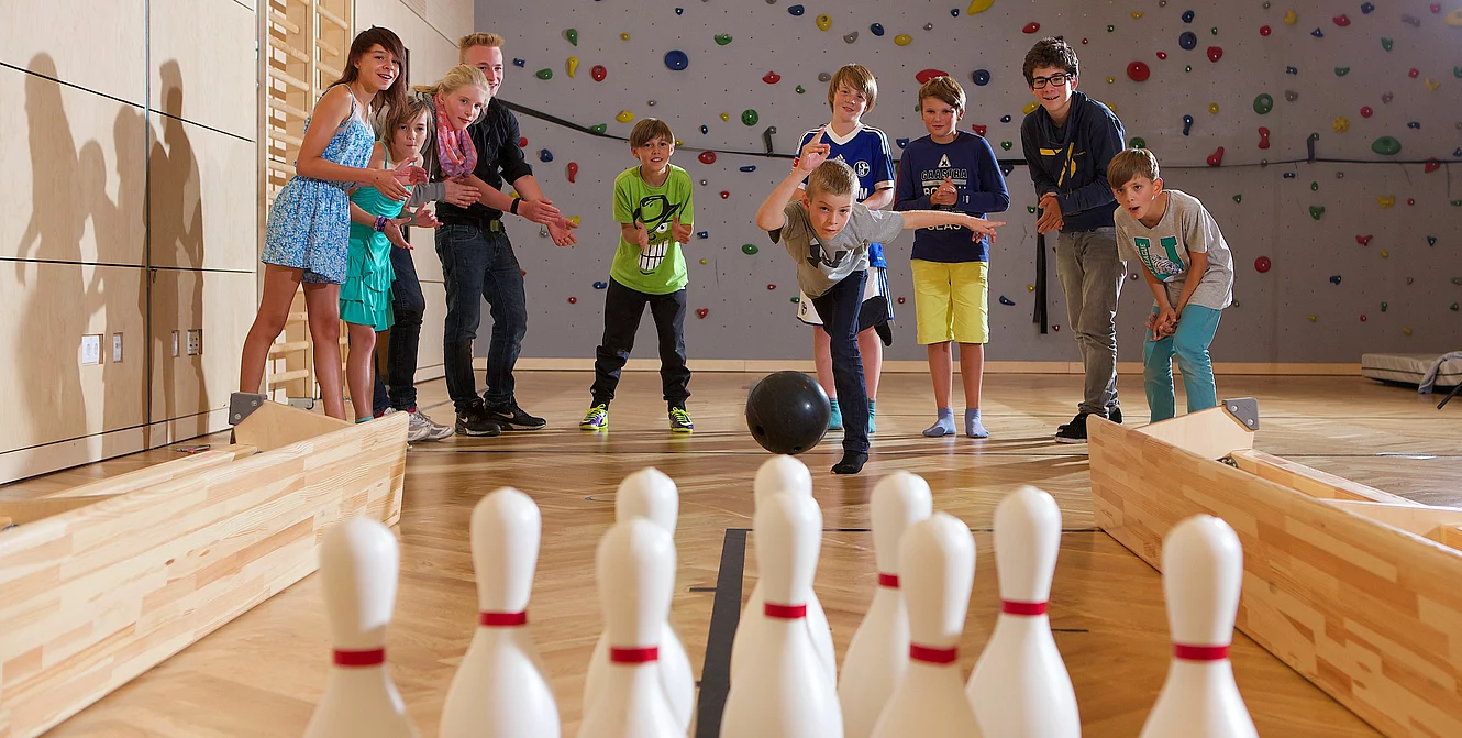 Kinder und Teenager kegeln in der Indoor Kletterhalle bzw. Sporthalle des Mountain Resort Feuerberg im Bergurlaub in Kärnten