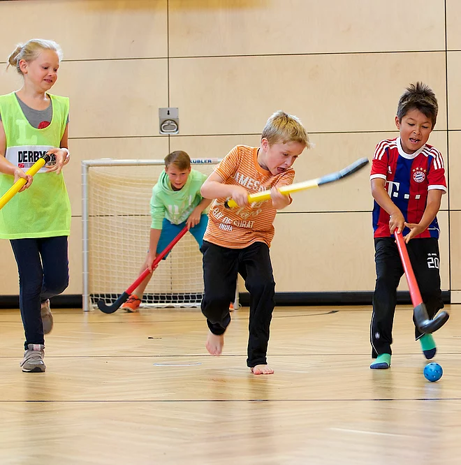 Kinder und Teenager spielen Hockey in der Indoor Kletterhalle bzw. Sporthalle des Mountain Resort Feuerberg im Bergurlaub in Kärnten