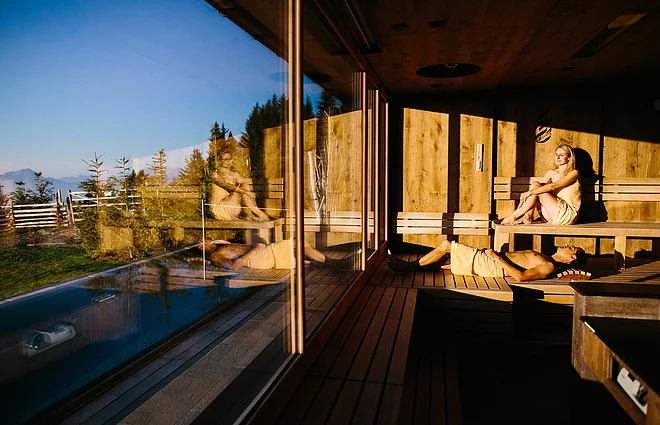 Menschen in der Konzertsaune genießen den Ausblick auf die umliegende Bergwelt im Wellnesshotel Feuerberg in Kärnten