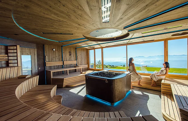 Menschen in der Konzertsaune genießen den Ausblick auf die umliegende Bergwelt im Wellnesshotel Feuerberg in Kärnten