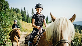 Mädchen reitet auf Pferd durch die Landschaft im Familienurlaub in Kärnten