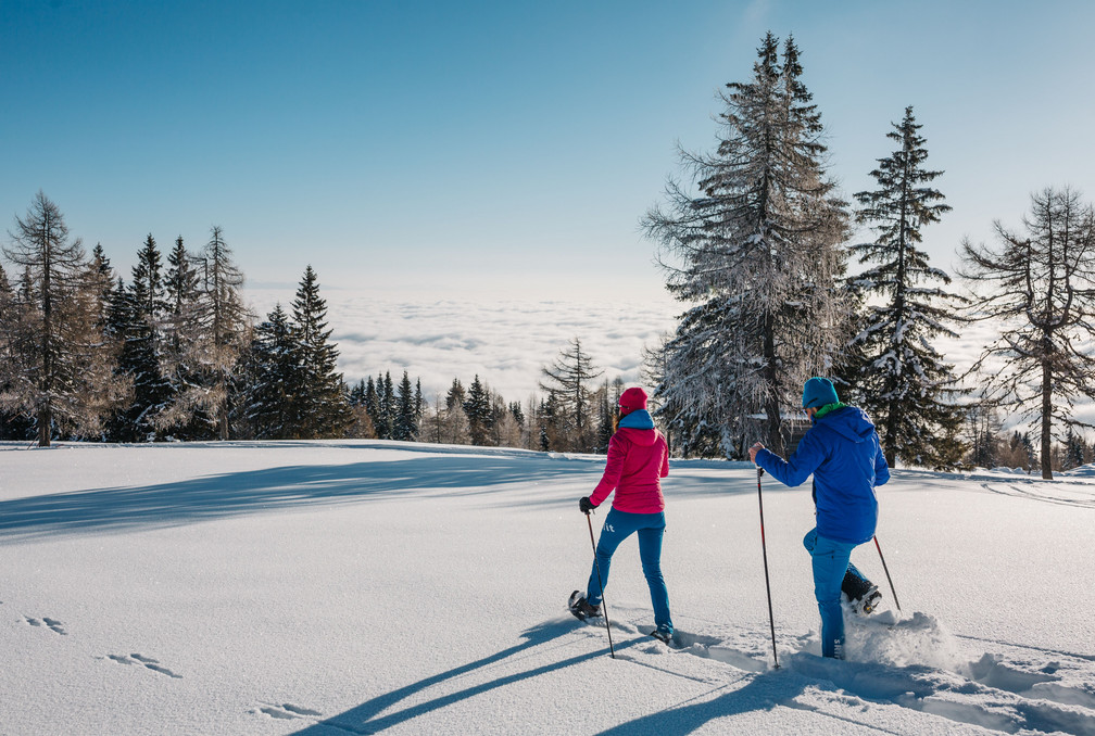 Mann und Frau beim Schneeschuhwandern durch eine verschneite Landschaft im Wellness- und Winterurlaub in Kärnten