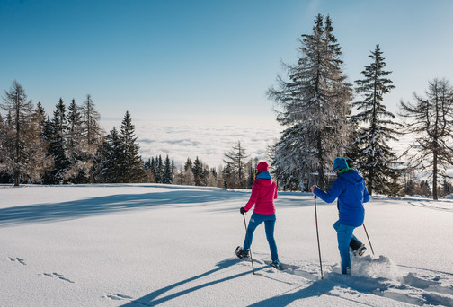 Mann und Frau beim Schneeschuhwandern durch eine verschneite Landschaft im Wellness- und Winterurlaub in Kärnten
