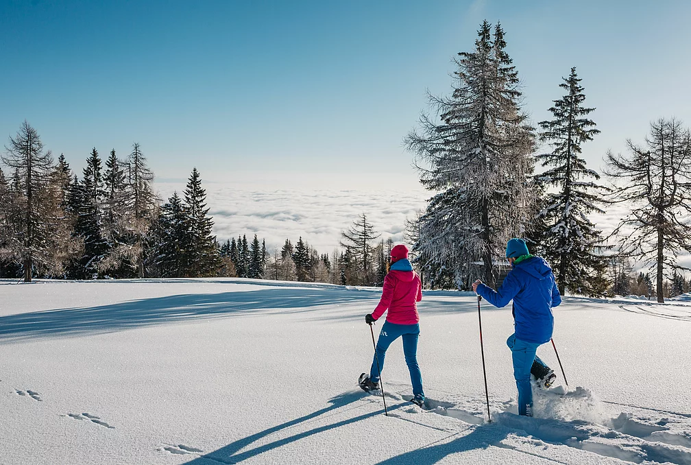 Mann und Frau beim Schneeschuhwandern durch eine verschneite Landschaft im Wellness- und Winterurlaub in Kärnten