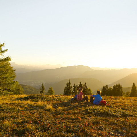 Mann und Frau sitzen nach dem Wandern im Sonnenuntergang auf einer Almwiese im Familienurlaub in Kärnten