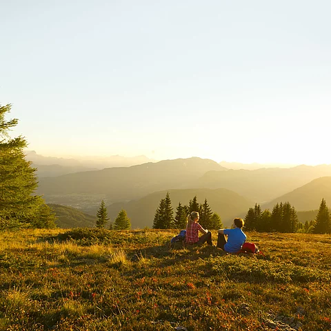 Mann und Frau sitzen nach dem Wandern im Sonnenuntergang auf einer Almwiese im Familienurlaub in Kärnten