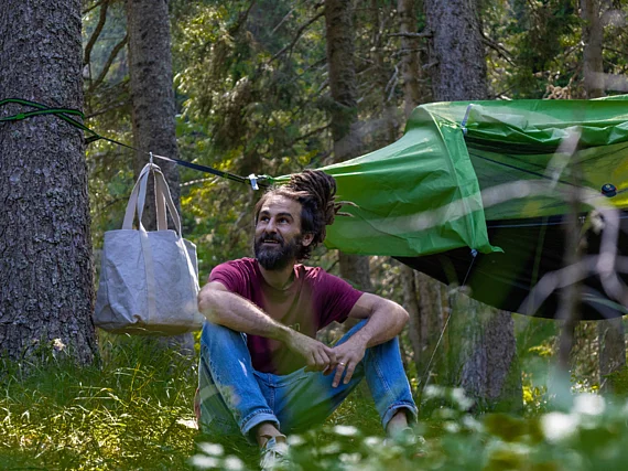 Waldschlafzimmer im Wald der Gerlitzen Alpe, zu sehen ein Mann der vor den Hängezelten sitzt und die Bergluft genießt