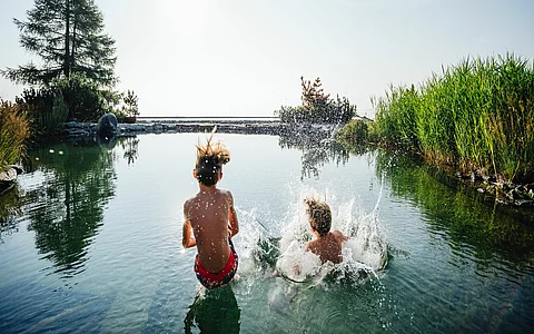 Kinder springen im Sommer in den Almsee des Family Spa Wellnesshotel Feuerberg in Kärnten