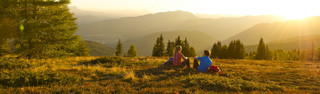 Mann und Frau rasten auf einer Wiese im Sonnenuntergang nach dem Wandern im Wanderurlaub in Kärnten