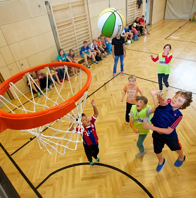 Kinder und Teenager spielen Basketball in der Indoor Kletterhalle bzw. Sporthalle des Mountain Resort Feuerberg im Bergurlaub in Kärnten